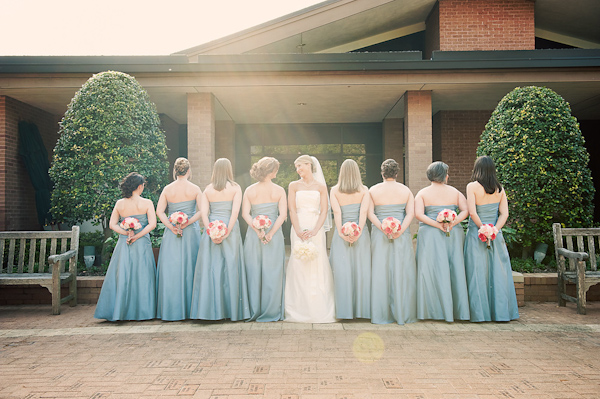 bride in middle of row of bridesmaids facing forward as bridesmaids face backwards holding their bouquets - bride is wearing white ball gown style dress and bridesmaids are wearing light blue dresses - photo by Houston based wedding photographer Adam Nyholt